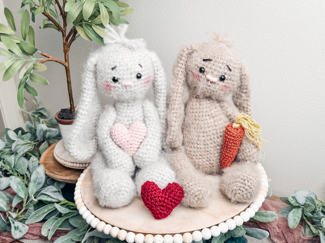 Be My Bunny crochet pattern: two fuzzy crochet bunnies, light gray with a pink heart and tan with a carrot, sitting on a wooden tray with a red heart