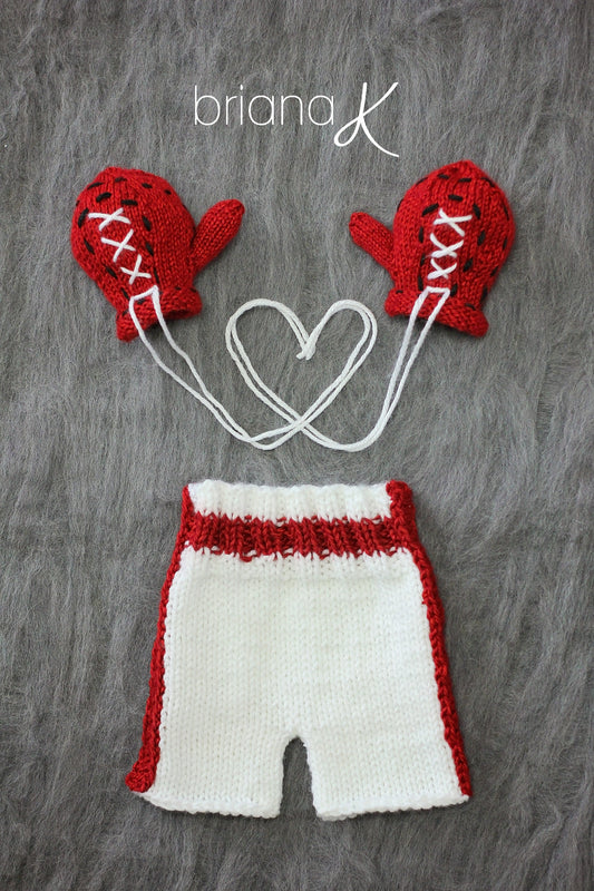 Red crochet baby boxing gloves with white laces and white shorts with red stripes on gray fur