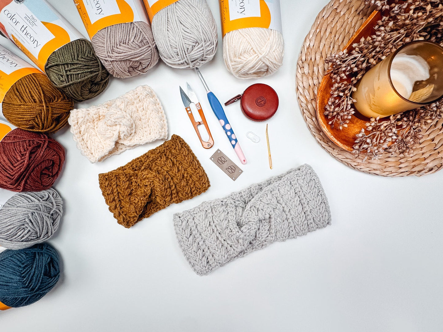 Yarn skeins, finished headbands, crochet tools, and a latte are displayed on a table adorned with decorative elements, alongside unique jewellery perfect for a handmade gift.