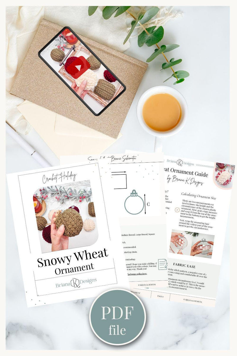 A smartphone and a cup of coffee rest on a table alongside an envelope, an eucalyptus sprig, and a printed PDF titled "Snowy Wheat Ornament," for making crocheted ornaments.
