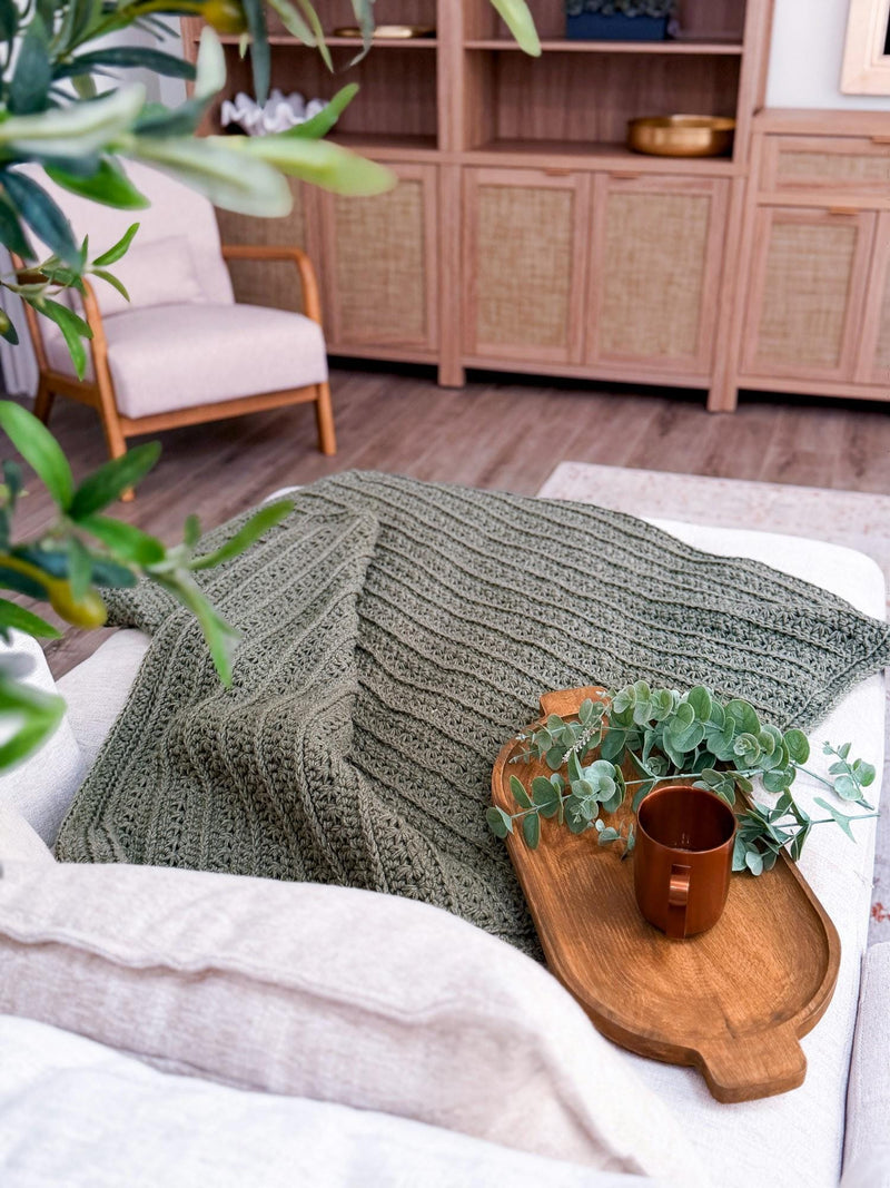 Sage green Petal Loop Stitch crochet blanket spread across a couch
