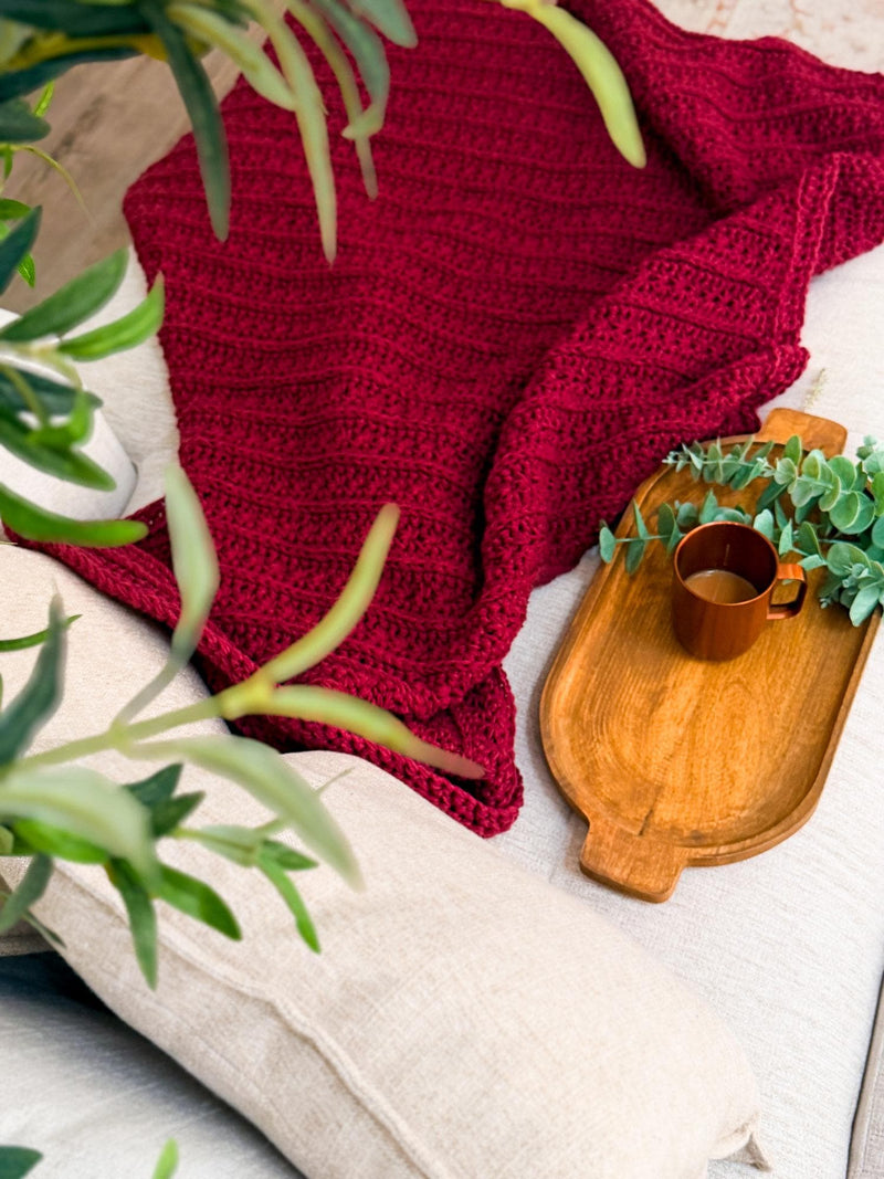 Deep red Petal Loop Stitch crochet blanket with a wooden tray and greenery