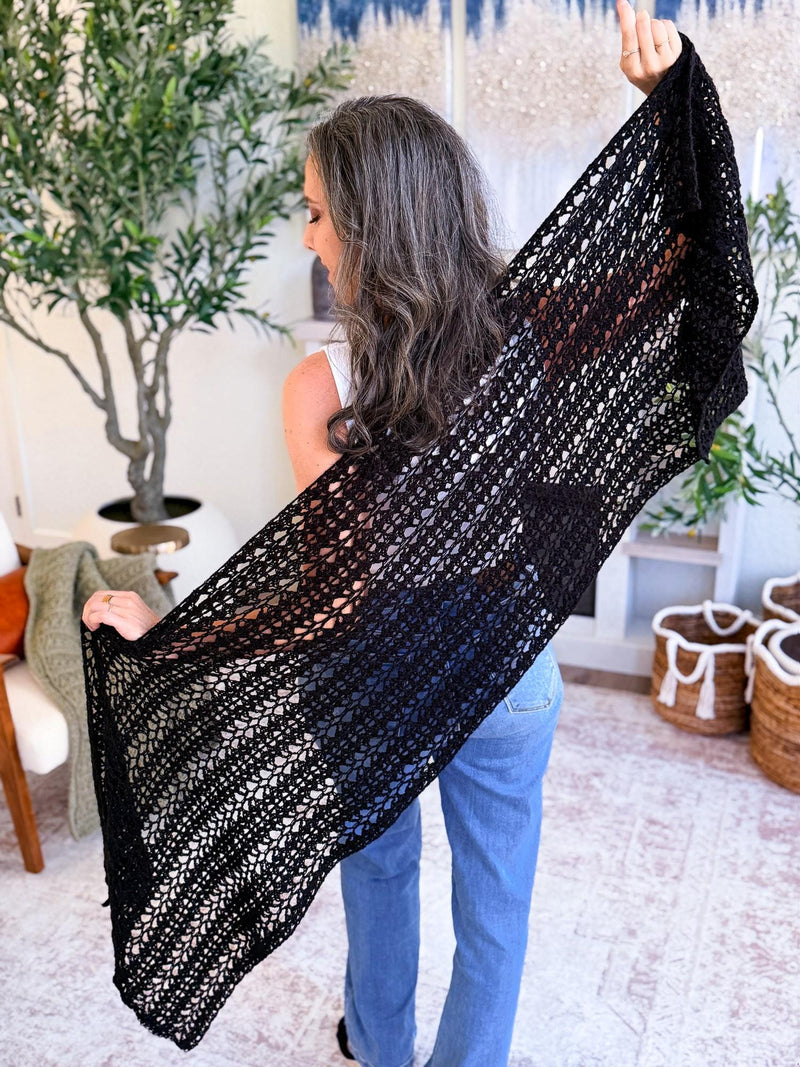Black mesh crochet wrap held up wide by a woman in jeans, seen from behind in a living room with plants