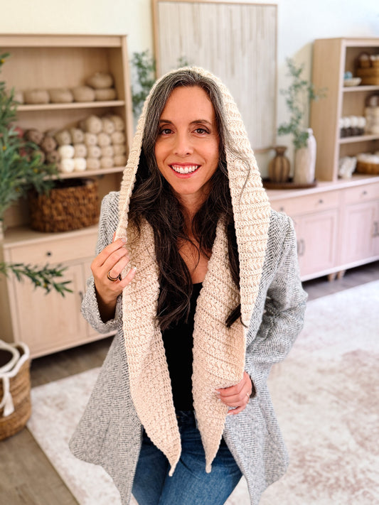 Smiling woman in the cream Wheat Stitch crochet hooded scarf, hood up, holding the edge of the hood
