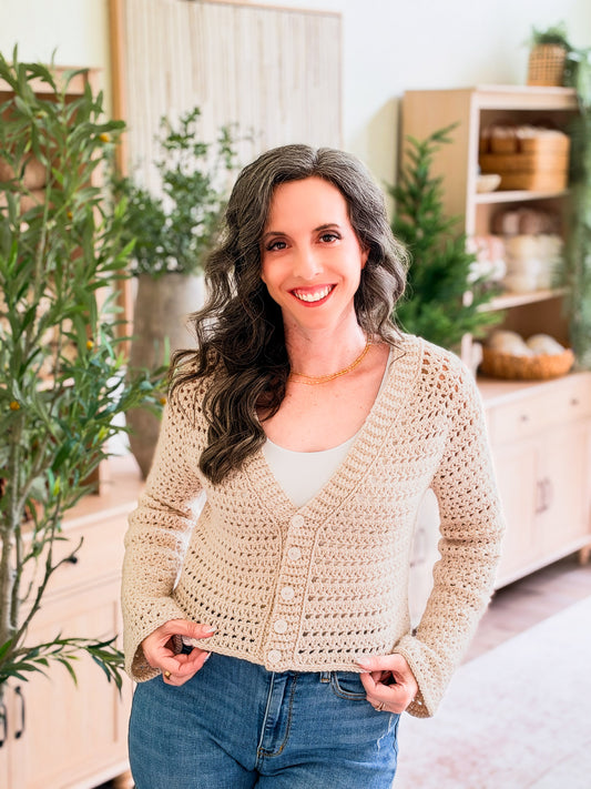 Breeze V-Neck Crochet Cardigan pattern: beige lacy V-neck crochet cardigan with buttons, cropped and worn by a smiling woman over a white top and jeans