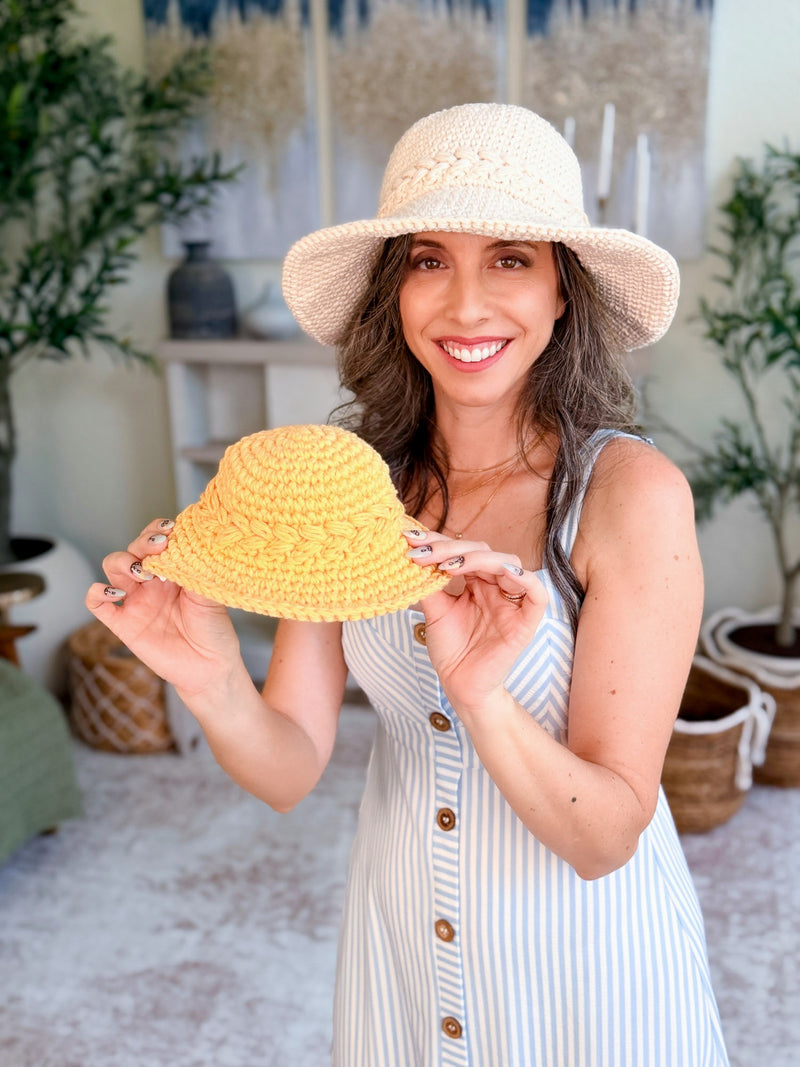Woman in a cream crochet sun hat holding up a small yellow child-size version