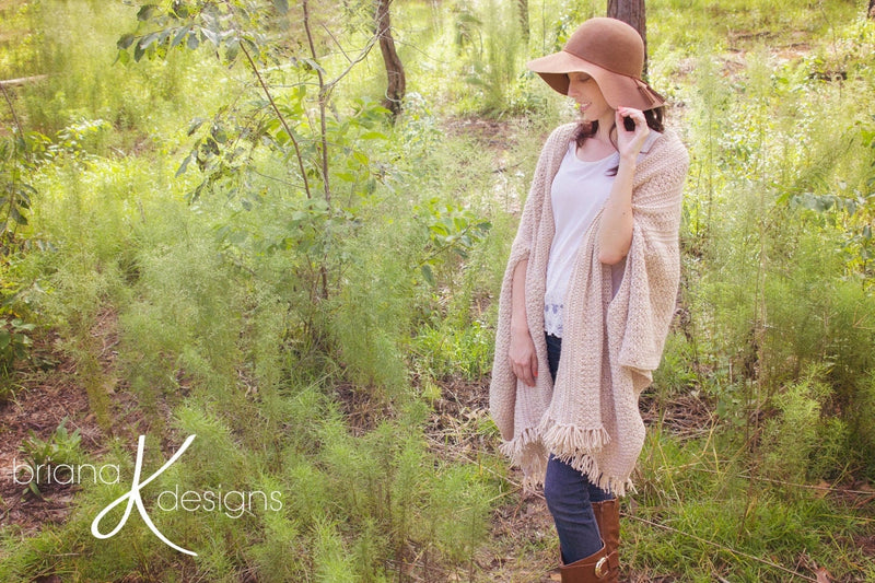 A woman wearing a cream crochet shawl wrap and hat, in a field of greenery.