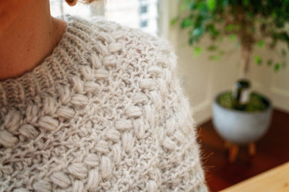 Close-up of a gray crochet sweater showing the puff stitch yoke and ribbed neckline