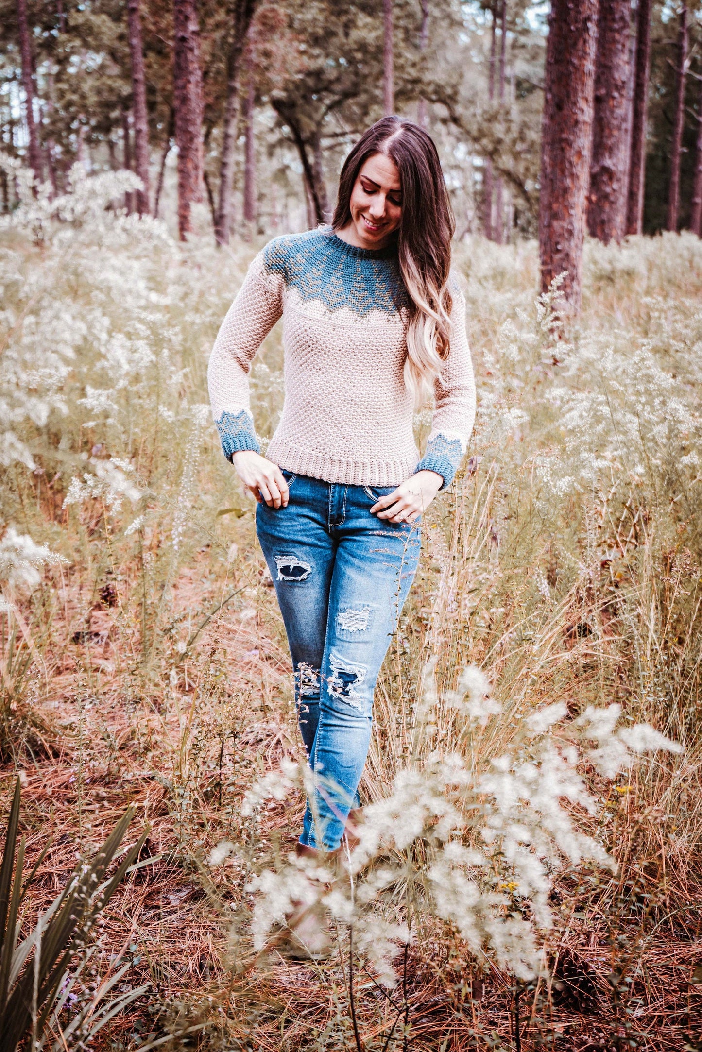 A person wearing a sweater and ripped jeans stands in a grassy area with trees in the background, showcasing unique jewellery that adds charm to their casual look.