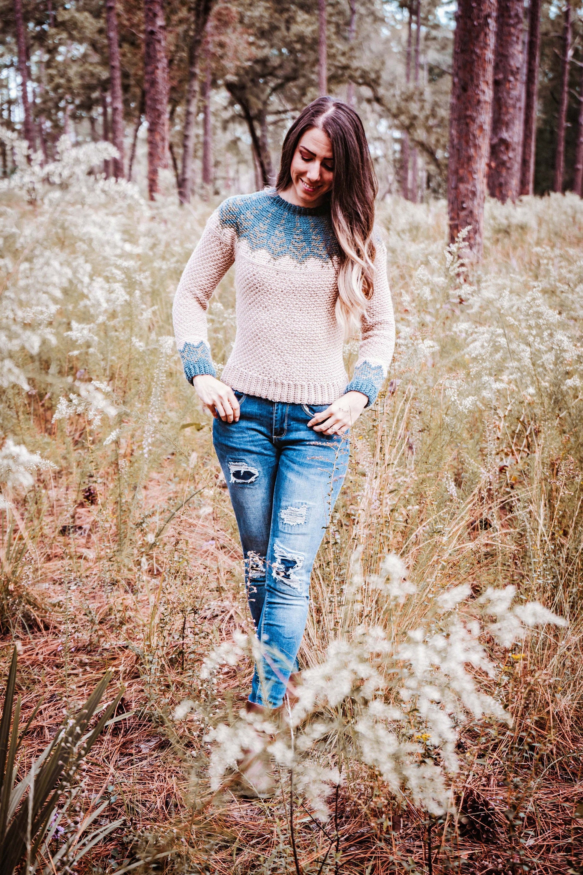 A person wearing a sweater and ripped jeans stands in a grassy area with trees in the background, showcasing unique jewellery that adds charm to their casual look.