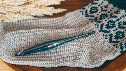 Close-up of a gray crochet sock foot showing ribbed texture with a blue crochet hook resting on top
