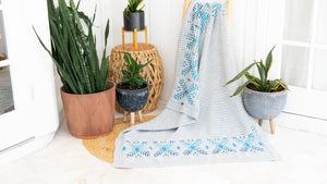 Gray crochet blanket with blue snowflake borders draped over a ladder among potted plants