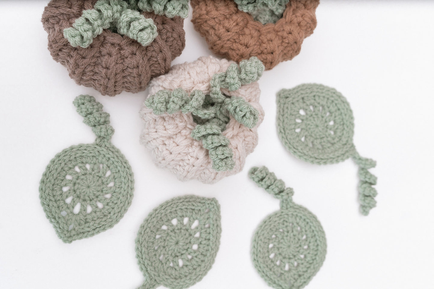 Several skeins of yarn in neutral colors and a crochet project featuring pumpkin and leaf designs, with a crochet hook placed on a white background.