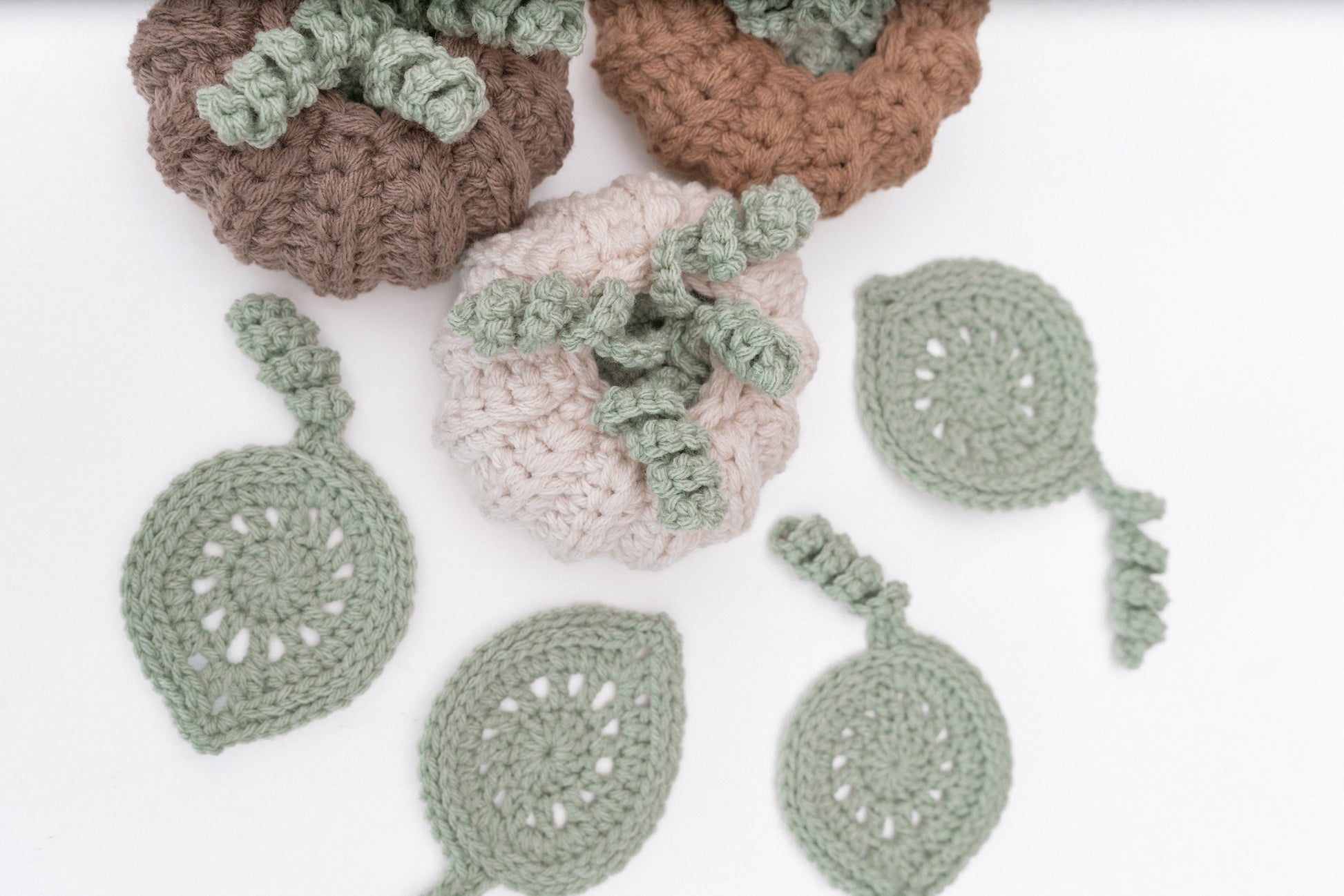 Several skeins of yarn in neutral colors and a crochet project featuring pumpkin and leaf designs, with a crochet hook placed on a white background.