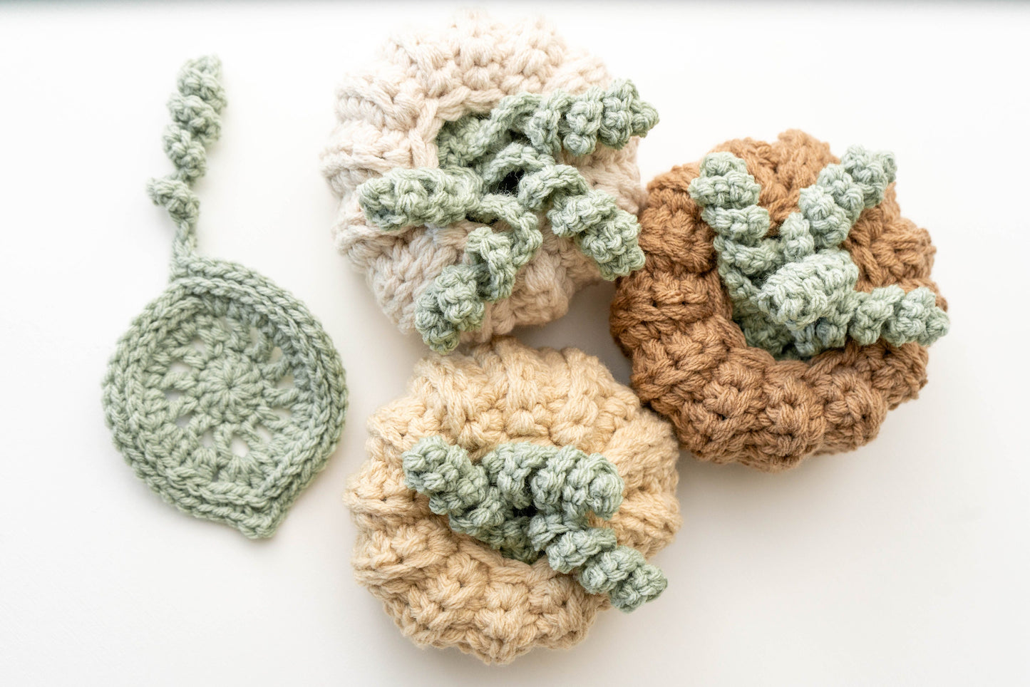 Several skeins of yarn in neutral colors and a crochet project featuring pumpkin and leaf designs, with a crochet hook placed on a white background.