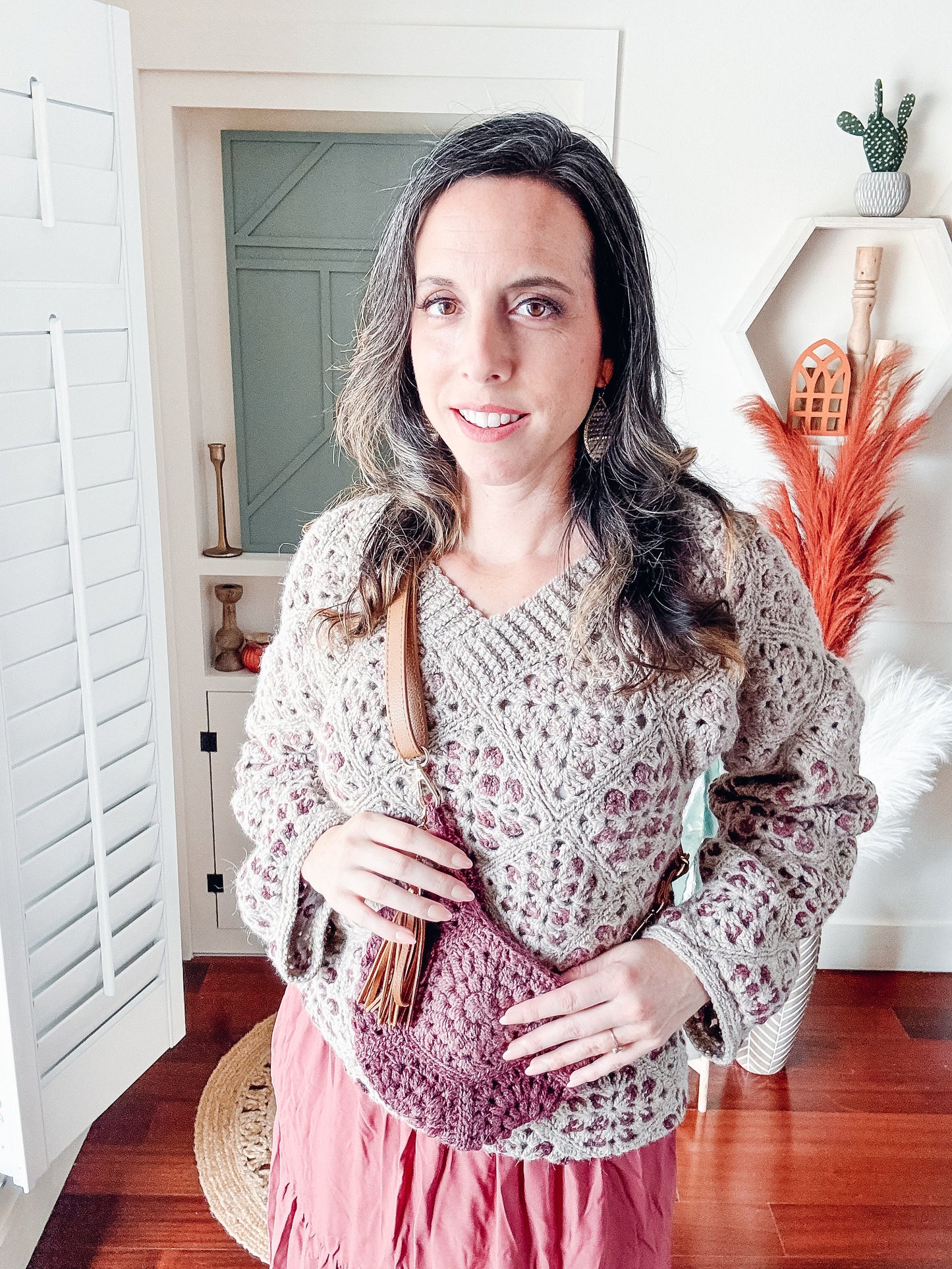 A woman wearing a vintage crochet sweater paired with a pink skirt, accessorized with unique handmade jewelry.