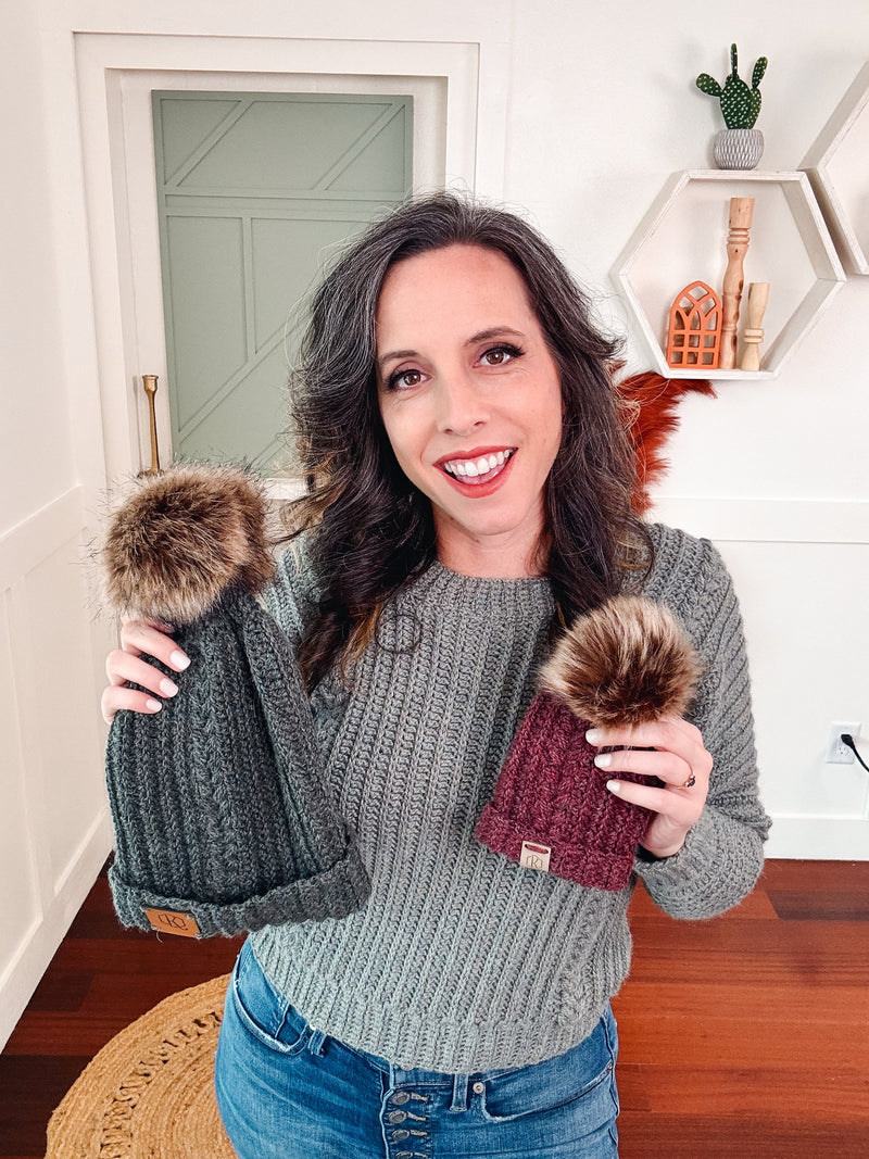 A woman showcasing two unique handmade pom pom beanie hats.