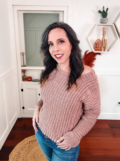 Dusty pink ribbed crochet sweater worn off one shoulder by a woman in jeans in a white room