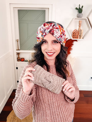 Woman wearing a chunky multicolor crochet ear warmer while holding a taupe one in front of her pink sweater