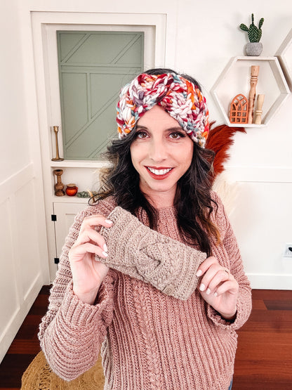 Woman wearing a chunky multicolor crochet ear warmer while holding a taupe one in front of her pink sweater