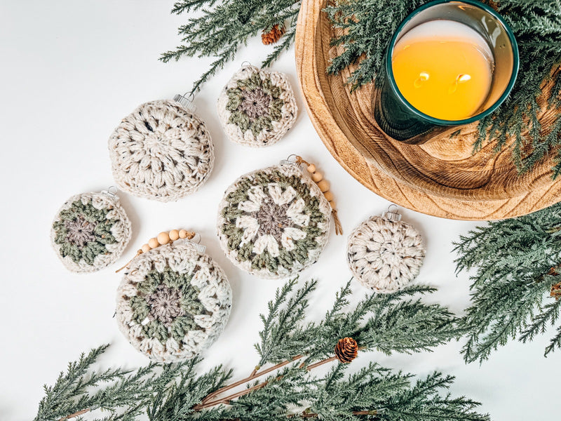 Handmade crochet christmas ornaments on a table next to a candle.