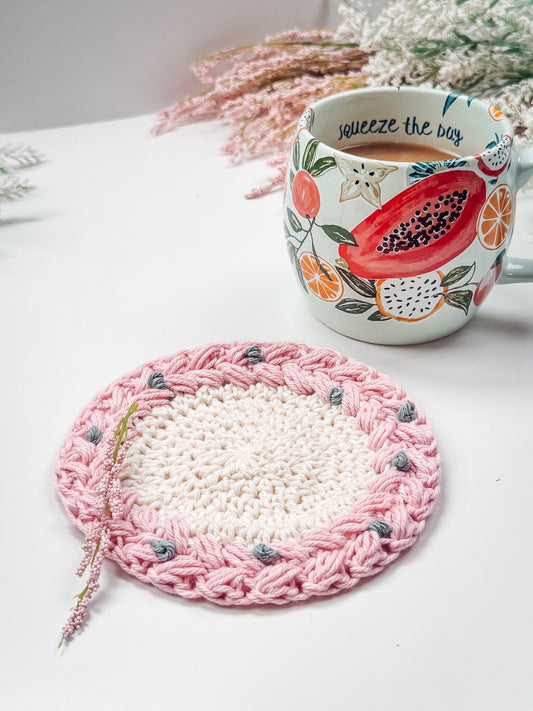 Wreath Ornament and Coaster - Crochet pattern: pink and cream crochet coaster with braided edge and gray bobbles beside a fruit print mug