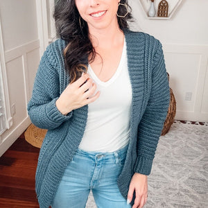 Close view of a slate blue crochet cardigan showing ribbed and textured stitches over a white top