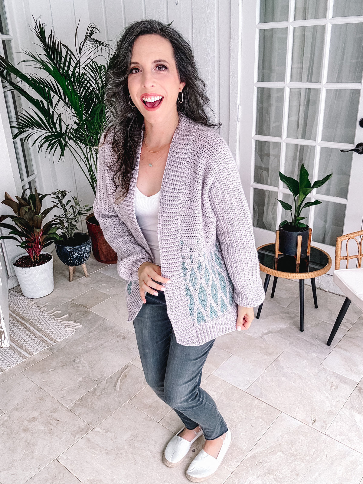 Woman in a cozy cardigan and jeans, adorned with unique jewellery, smiling indoors.