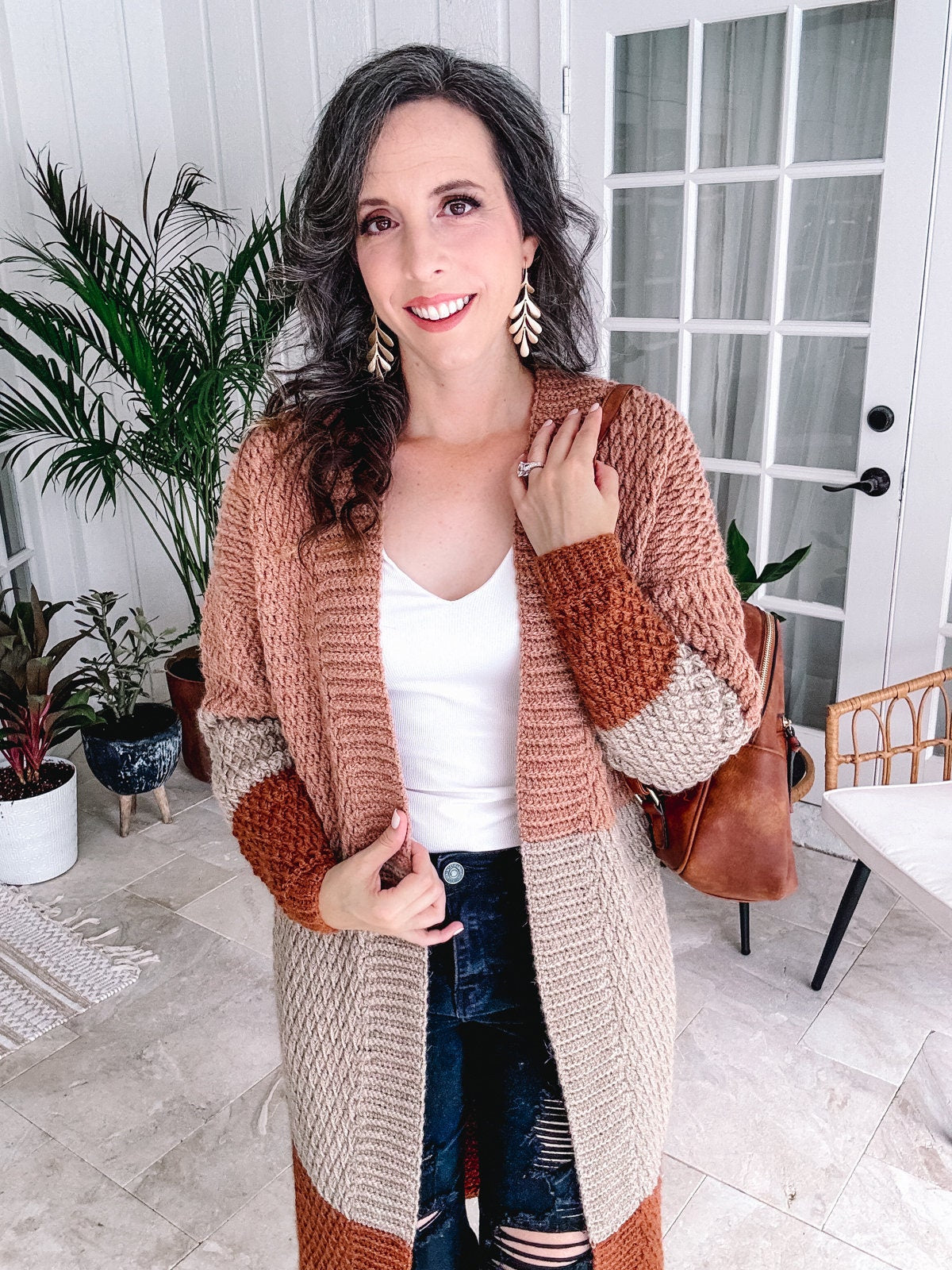 Woman in a stylish striped cardigan and unique jewellery posing for the camera in an elegantly decorated room.