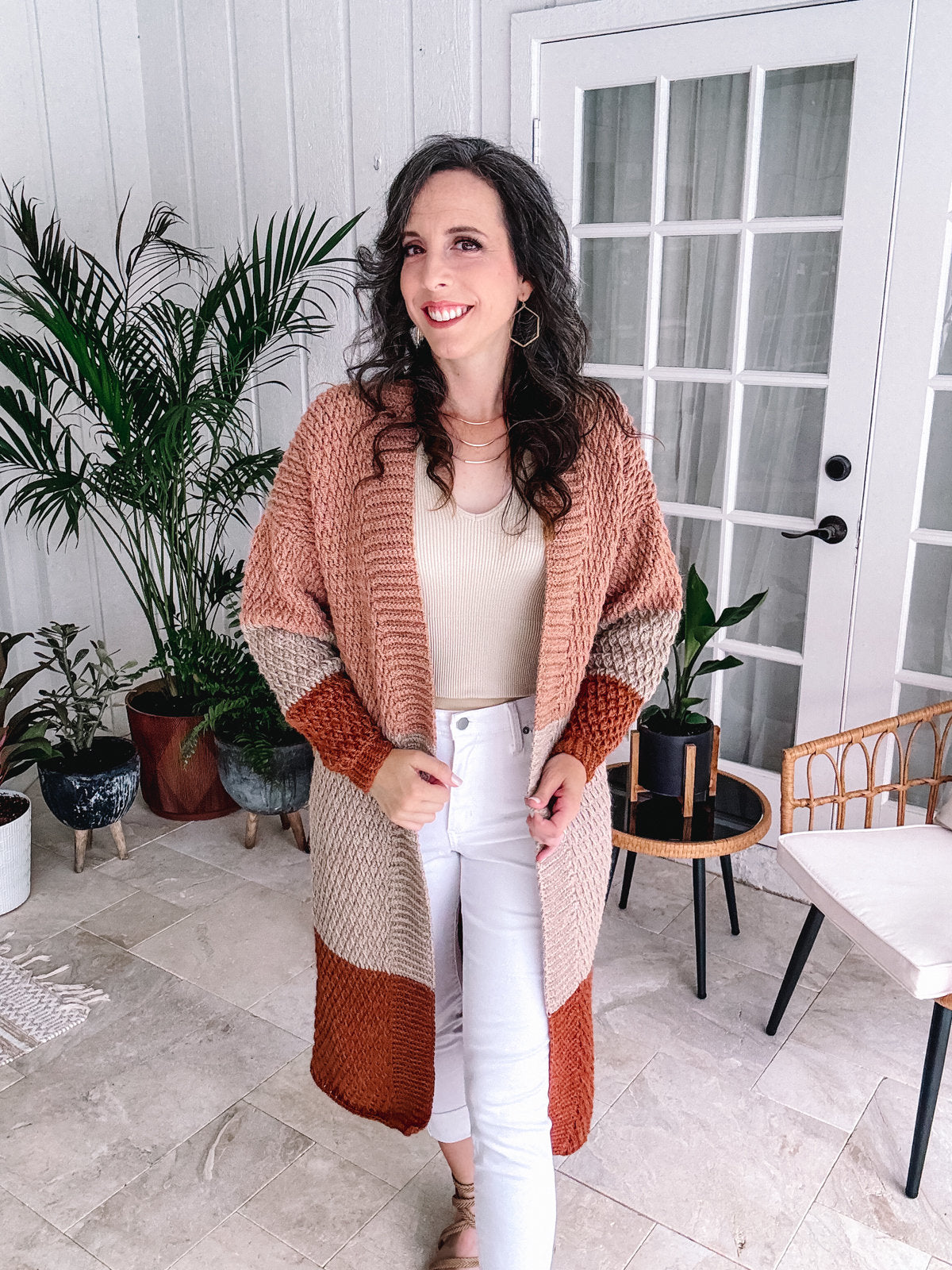 Woman in a cozy cardigan and unique jewellery posing in a stylish interior.