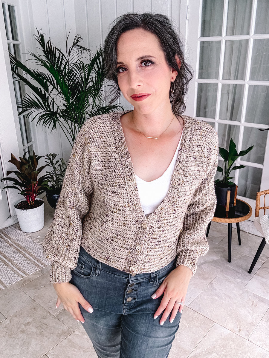 Woman in a beige cardigan and jeans standing in a bright room, holding a handmade gift.