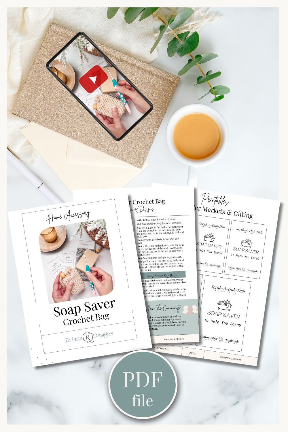 A tabletop display featuring crochet project sheets, a cup of coffee, a smartphone showing a crochet video, and a notebook. The visible header reads "Soap Saver Crochet Bag" and a label indicates a PDF file.