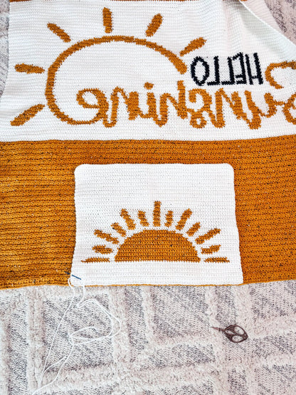 Crochet blanket and sun pillow panel laid flat on a rug with loose yarn and scissors, showing the wrong side
