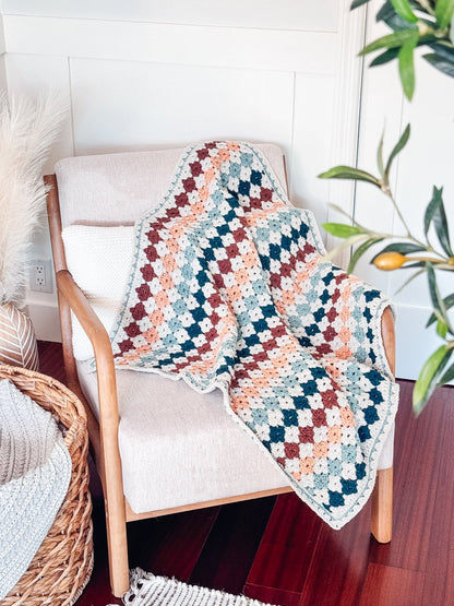 Crochet granny stitch blanket in rust, peach, teal and cream draped over a cream armchair