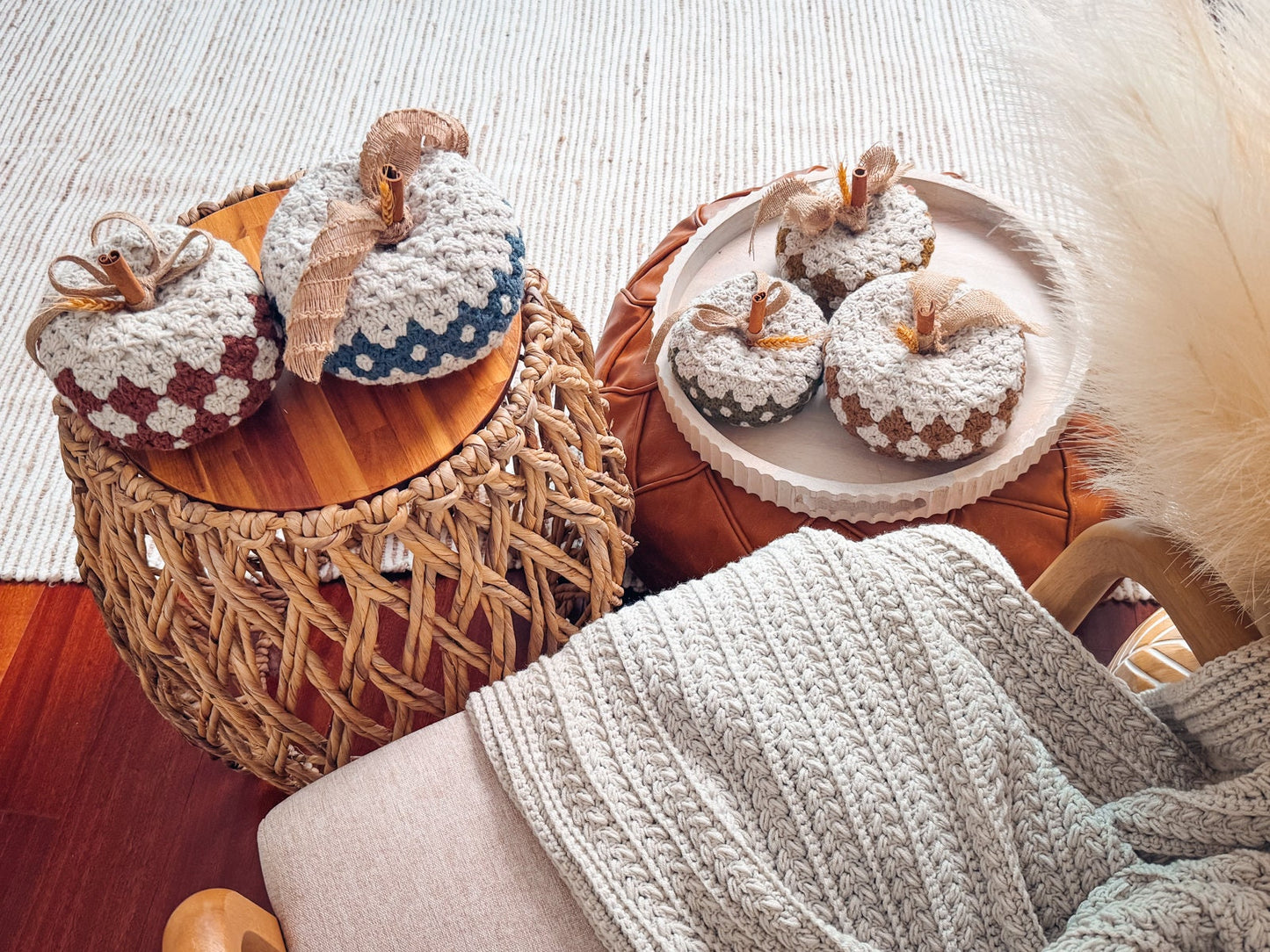 A cozy scene with yarn pumpkins on wicker and wooden stools, alongside a knit blanket, and adorned with unique jewellery.