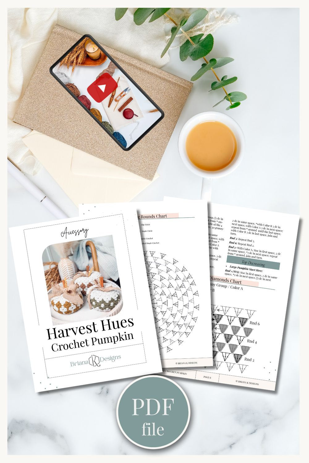 Top view of a workspace with crochet yarn on a tablet, a cup of coffee, a notebook, eucalyptus leaves, and three printed crochet pattern sheets with a PDF file label. This cozy setup is perfect for creating handmade gifts.