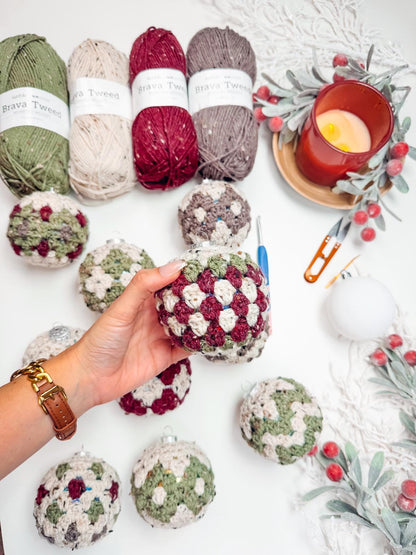 A hand holds a crocheted ornament above a table adorned with colorful yarns, a candle, and crochet tools — the perfect scene for crafting a handmade gift.