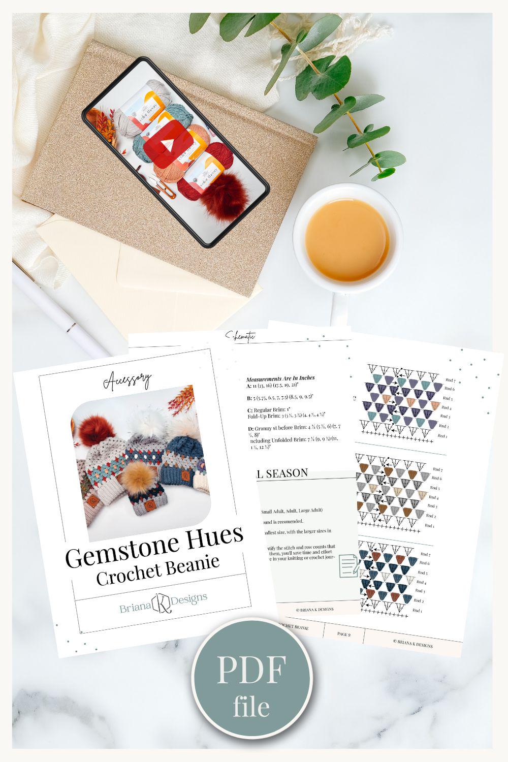 Top view of a coffee cup, phone with yarn image, envelope, green leaves, and a crochet beanie pattern titled "Gemstone Hues," perfect as a handmade gift.