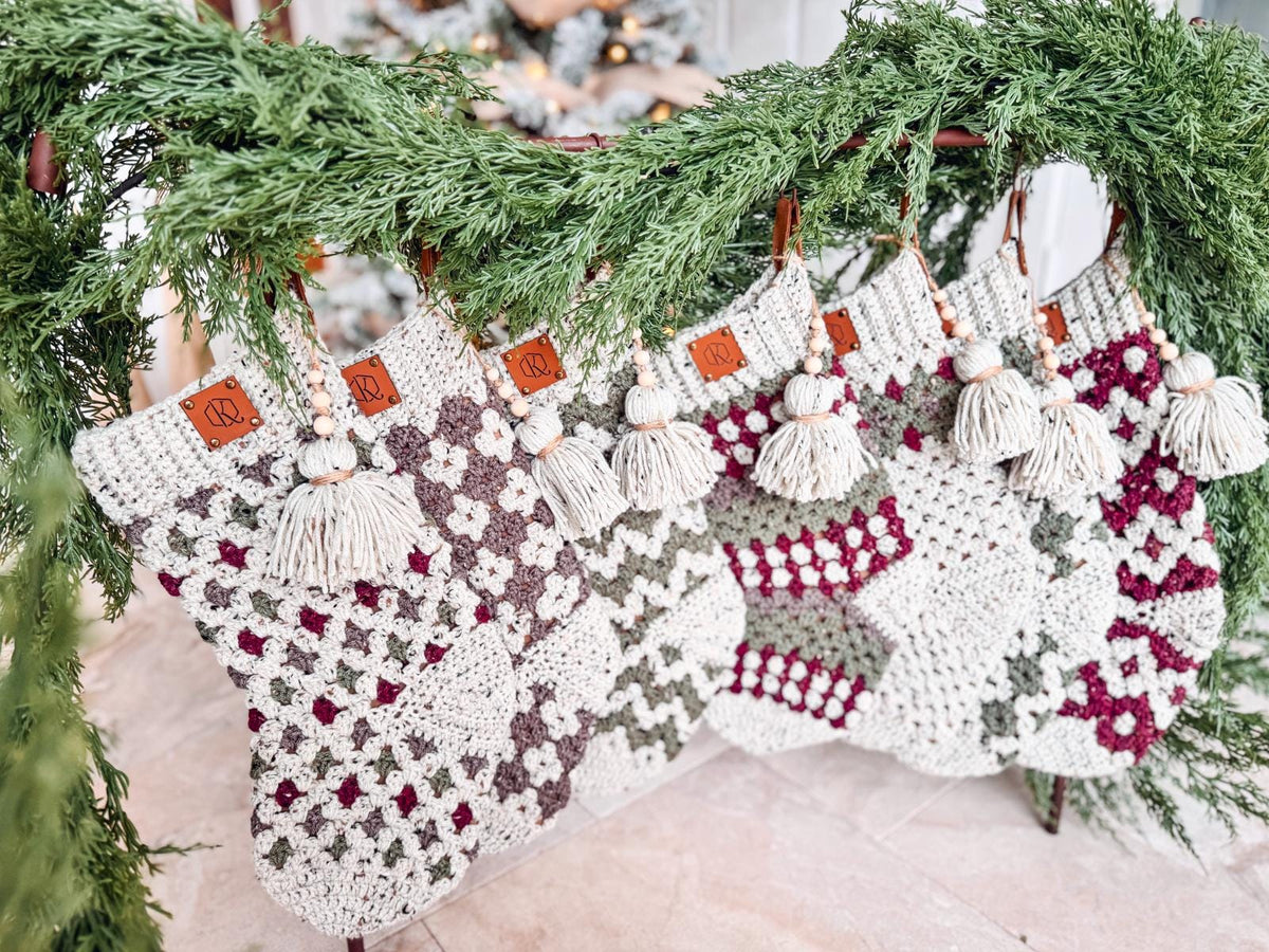 Several crocheted stockings with tassels hanging from a garland, featuring various patterns in green, red, and white—perfect as a handmade gift to complement your vintage clothes collection.