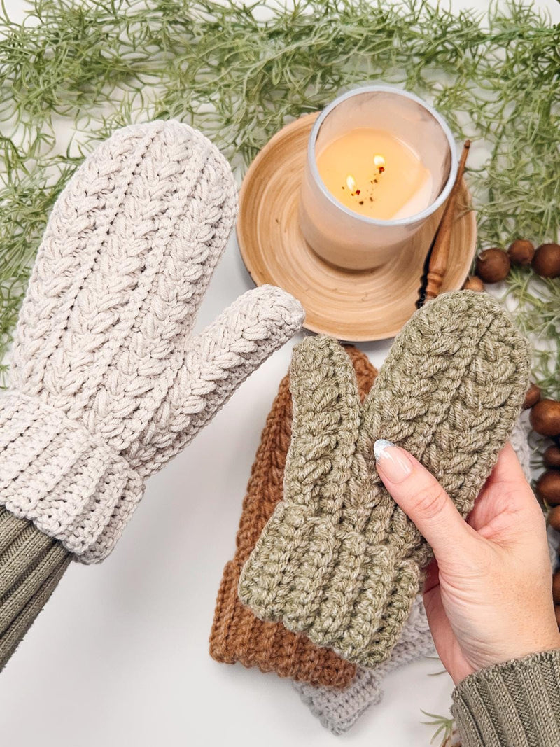 Light gray crochet mitten worn on one hand while the other hand holds a small sage green mitten