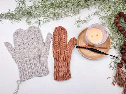 Light gray and rust crochet mittens laid flat, unseamed, beside a candle and a dark crochet hook