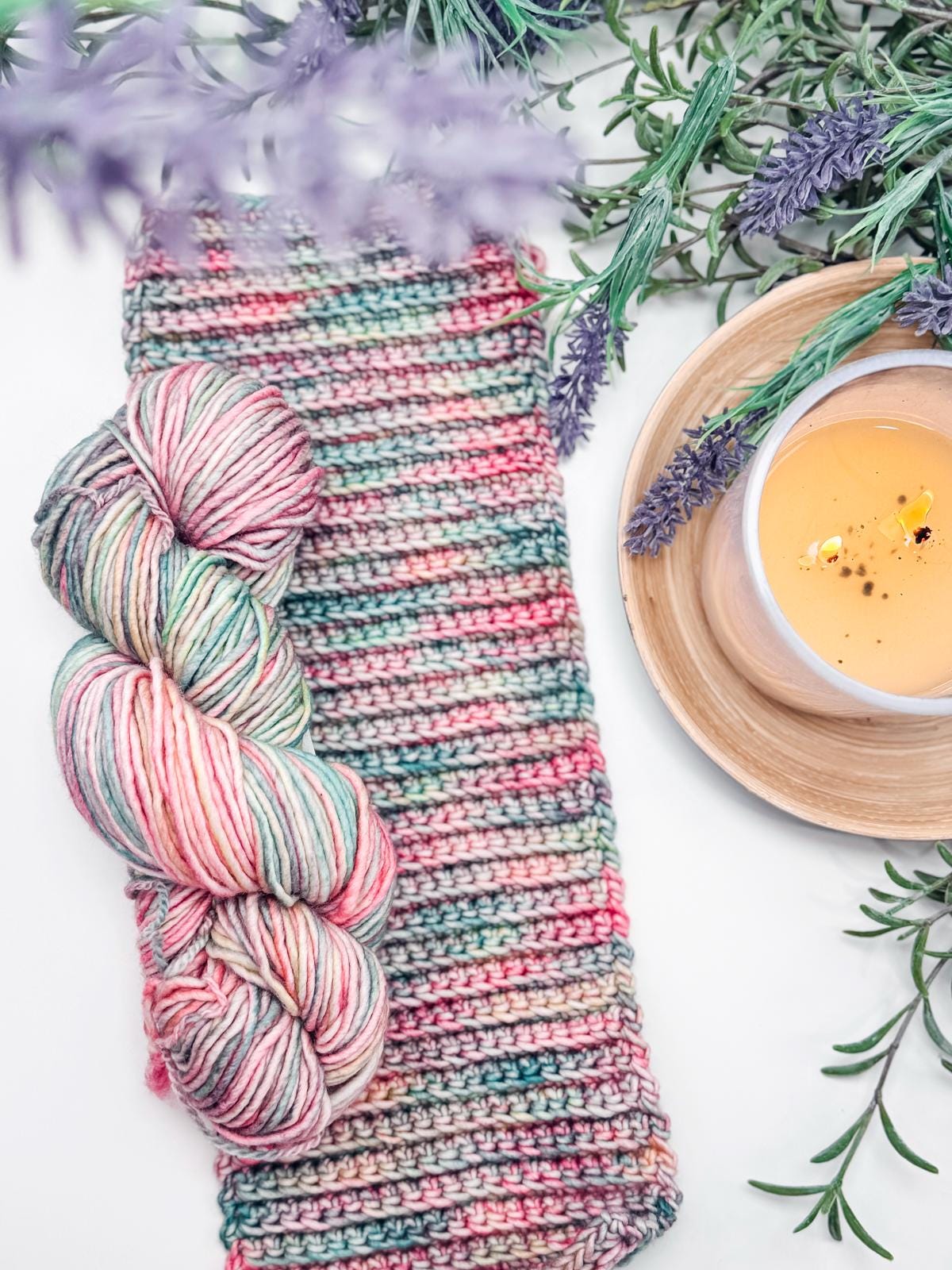 A delightful crochet project with colorful yarn, paired with a yarn skein, lavender sprigs, and a steaming cup of coffee on a wooden saucer. This scene could inspire the perfect handmade gift for someone special.