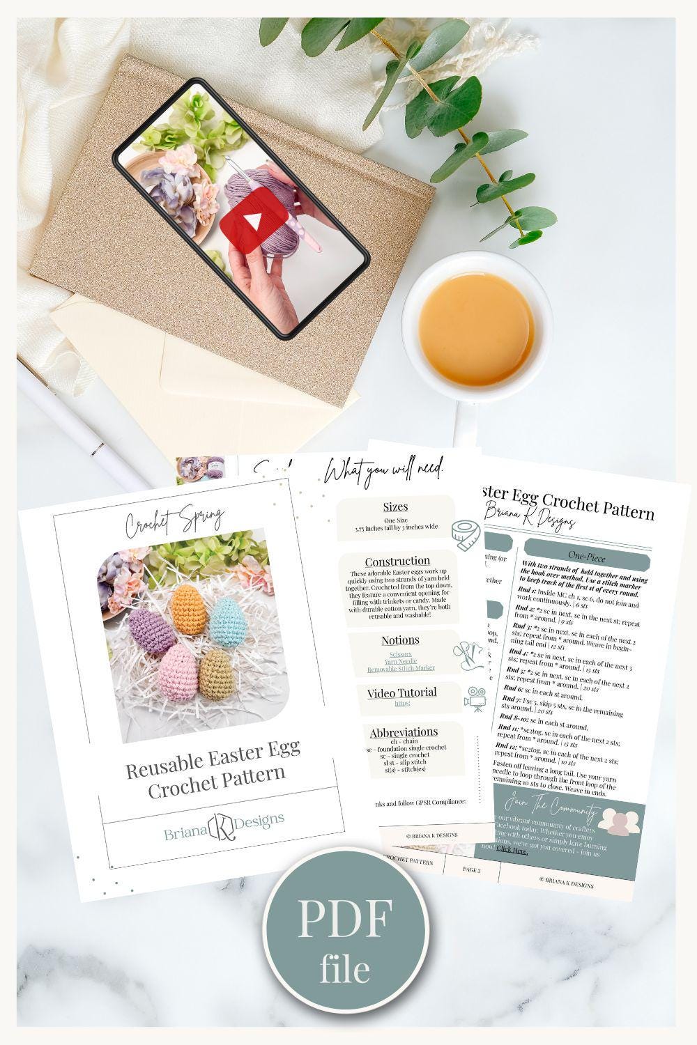 Flat lay of crochet pattern materials including a printed PDF, a smartphone displaying a video, a cup of coffee, and green foliage on a white surface—perfect inspiration for creating a handmade gift.