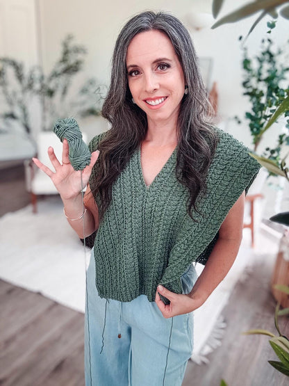 Green crochet top in progress with open sides, worn by a smiling woman holding a skein of matching green yarn