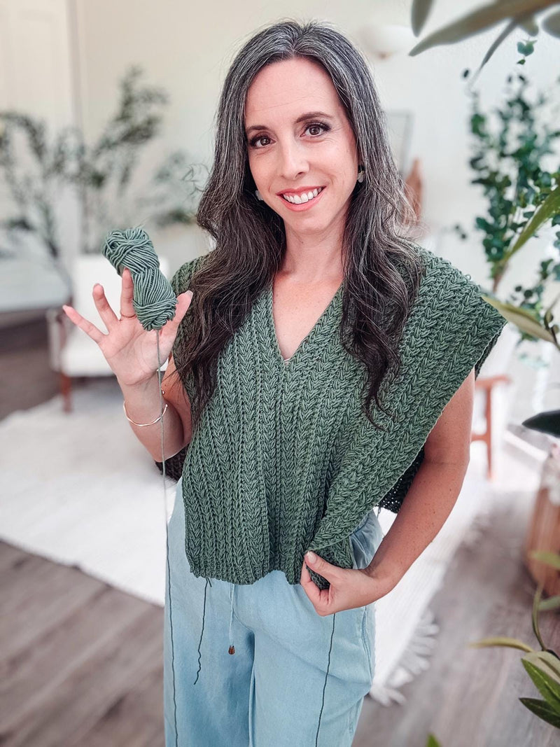 Green crochet top in progress with open sides, worn by a smiling woman holding a skein of matching green yarn