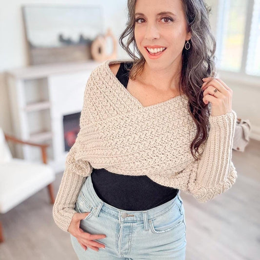 Woman with long hair in a cream  sweater and jeans poses indoors, smiling, showcasing unique jewellery.