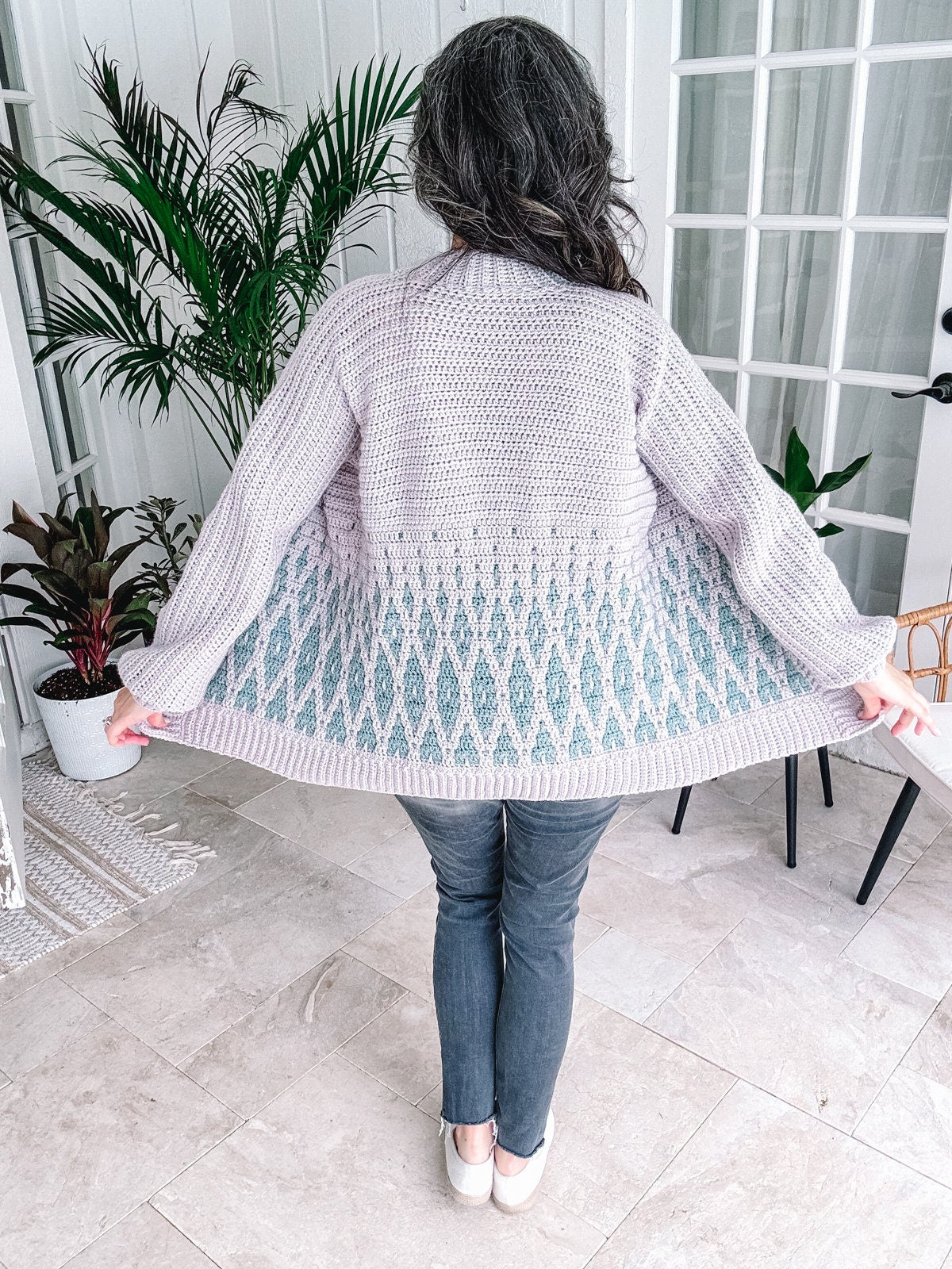 Woman showing off the back of her light-colored, handmade crochet cardigan indoors.