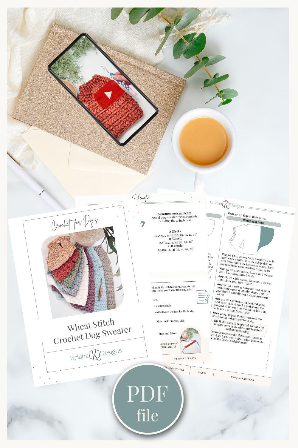 Flat lay of crochet dog sweater pattern printouts, a phone showing a crochet video, an envelope, a cup of coffee, a pen, and a sprig of greenery.
