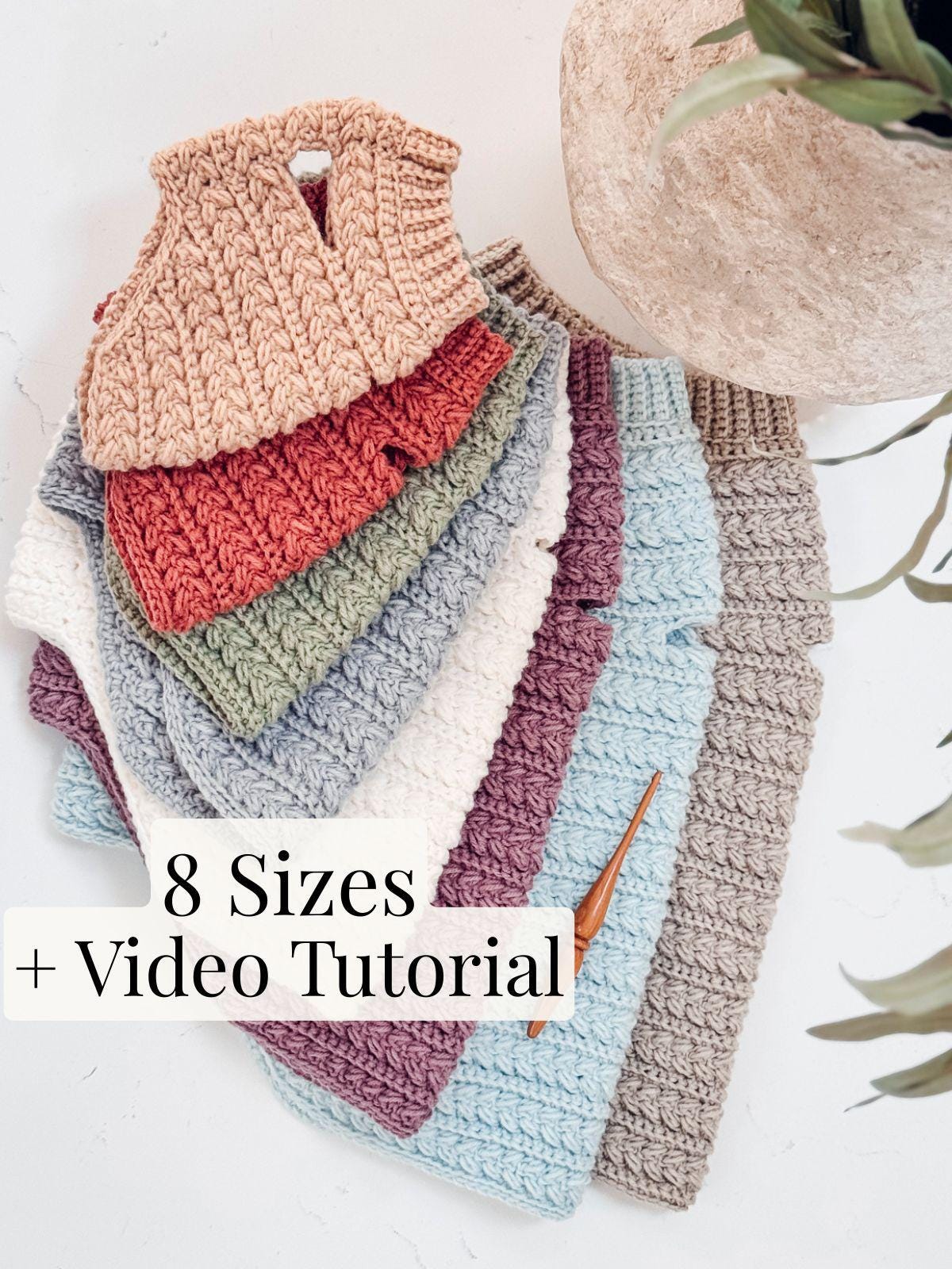 Stack of eight crocheted sweaters in various colors displayed next to a crochet hook, perfect as a handmade gift. Text reads "8 Sizes + Video Tutorial.