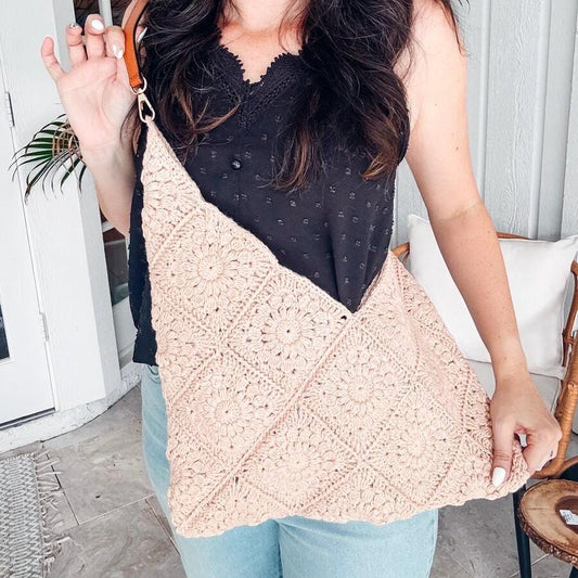 A woman in a black top and jeans holds a beige, crocheted handbag, showcasing her flair for vintage clothes. She is standing indoors near a white door.
